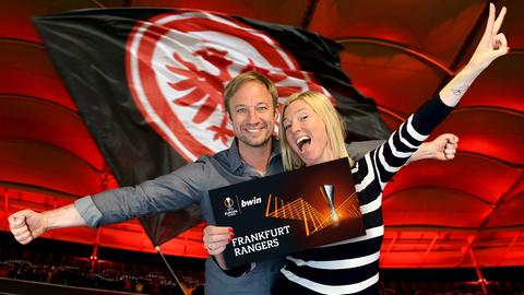 Tobi und Tanja halten vor dem Hintergrund der Eintracht-Fahne aufgeregt einen Ticketgutschein in die Kamera