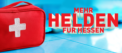 Eine Erste-Hilfe-Tasche steht auf blauem Fliesenboden. Daneben steht in roter Schrift "Mehr Helden für Hessen".