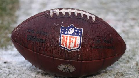 Ein Football mit Logo der NFL liegt auf einem Spielfeld.