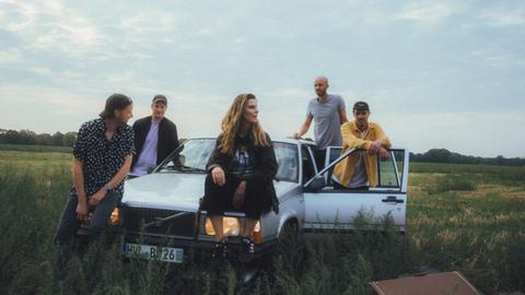 Die Band Juli sitzt auf einem Auto in einem Feld.