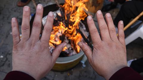 Eine Frau wärmt sich die Hände an einem Feuer, während sie vor ihrem eingestürzten Wohnhaus wartet. Internationale Rettungskräfte strömen in die Türkei, um die betroffene Region zu unterstützen.