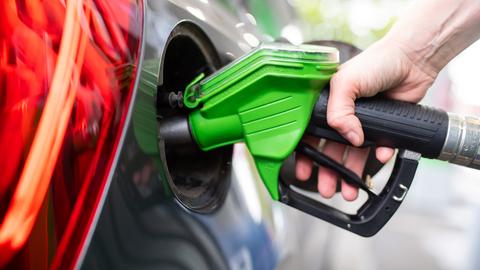 Eine Frau hält an einer Tankstelle an einer Zapfsäule eine Zapfpistole in der Hand und betankt ein Auto .