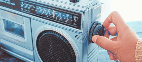 Eine Hand dreht den Regler an einem alten Radio.