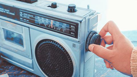 Eine Hand dreht den Regler an einem alten Radio.