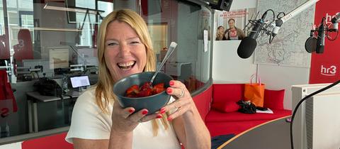 Tanja hält grinsend die Schüssel voller Erdbeeren in die Kamera