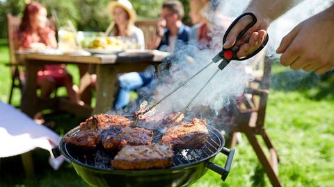 Ein Mann wendet Fleisch auf dem Grill.